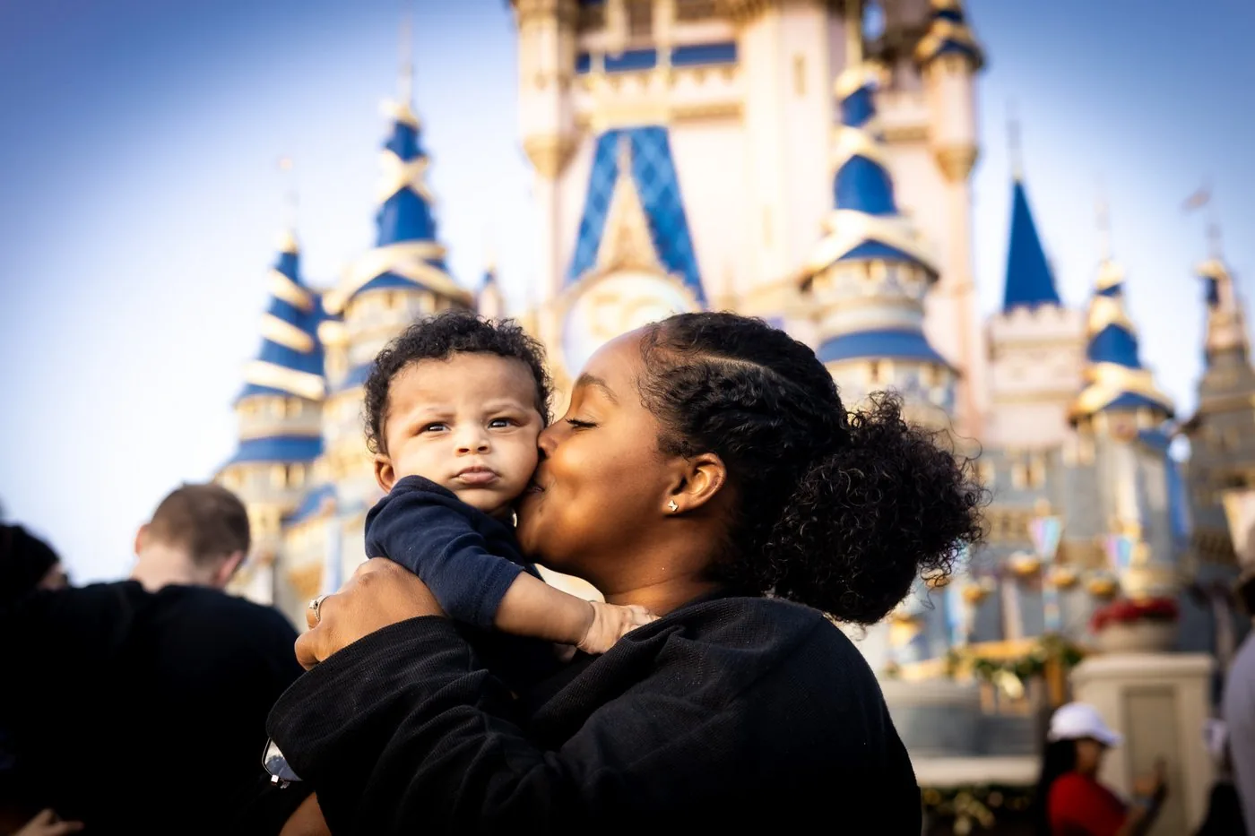 Ashly Roberson kissing a newborn baby in front of Cinderella Castle at Magic Kingdom Walt Disney World