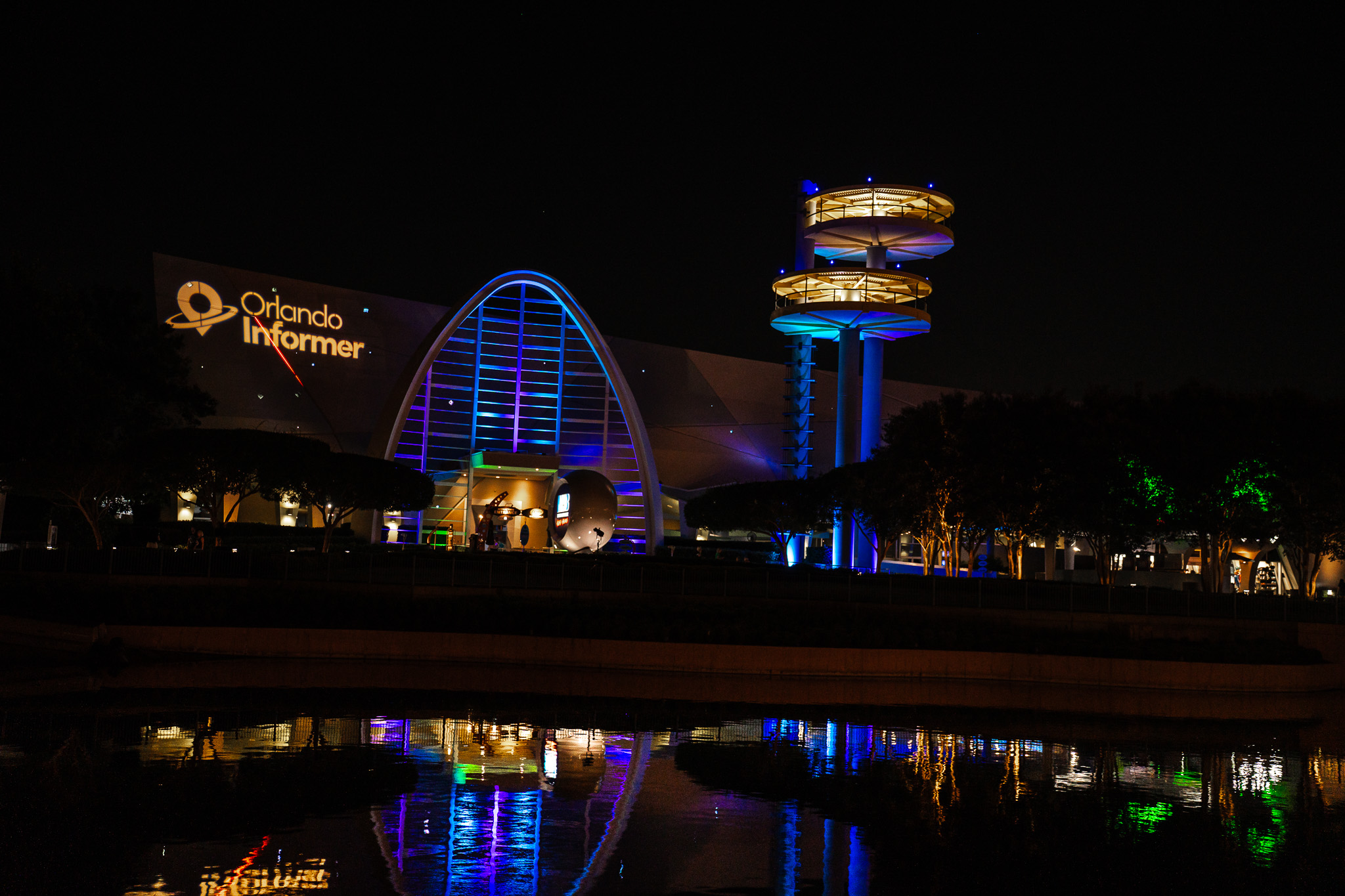 Orlando Informer logo projected on Universal Studios Florida at night with a reflection in the water
