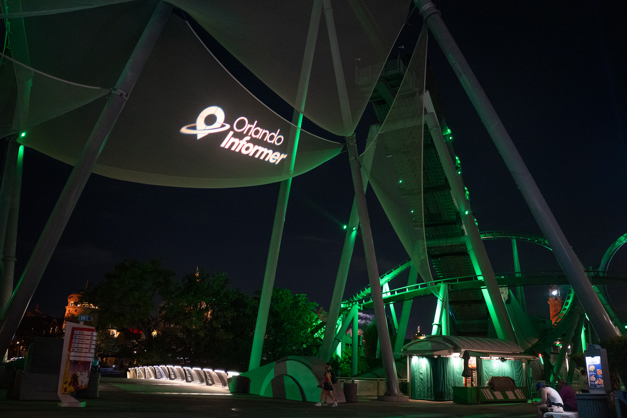 Orlando Informer logo projected on the tent canopy near the Incredible Hulk coaster lit in green at night during the meetup